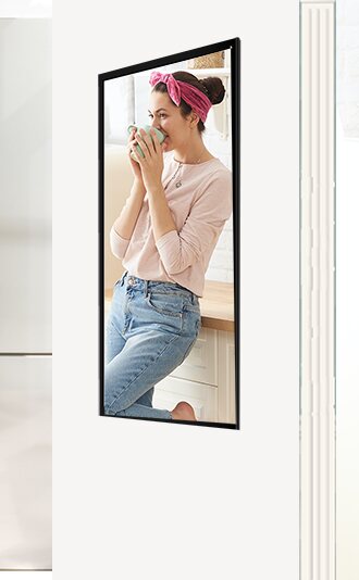 A tall screen on a wall showing a woman in a pink headband drinking coffee in her own kitchen.